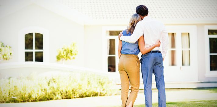 Rear view of couple standing with arm around outside the house