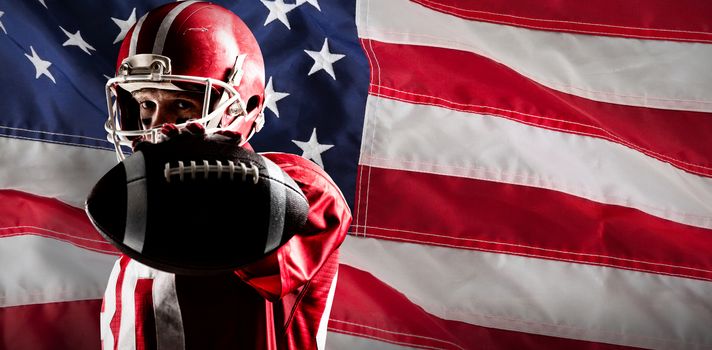 American football player holding rugby ball against close-up of an american flag