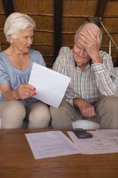 Front view of worried senior couple discussing over medical bills in living room at home