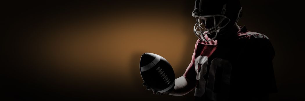 American football player standing with rugby ball and helmet against orange background with vignette