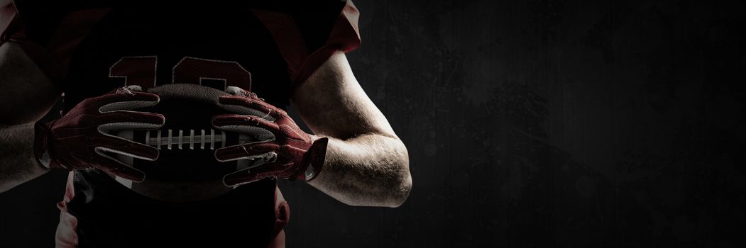 American football player holding rugby ball against full frame shot of grunged concrete wall