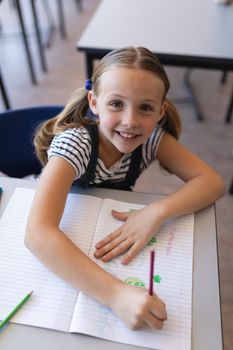 High angle view of schoolgirl looking at camera at desk in classroom of elementary school