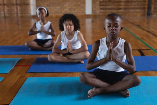 Front view of schoolkids doing yoga and meditating on a yoga mat in school