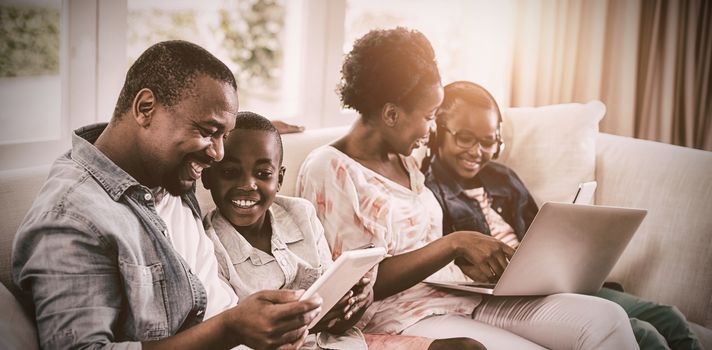 Smiling parents and kids using laptop and digital tablet on sofa at home