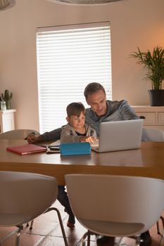 Front view of caring father helping his son with his homework while using laptop at home