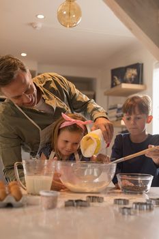 Front view of loving father with his sweet children preparing cookies in kitchen at home