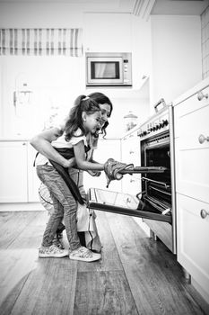 Mother and daughter placing tray of cookies in oven at kitchen