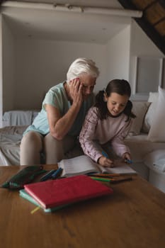 Front view of a grandmother helping her granddaughter with homework in living room at home