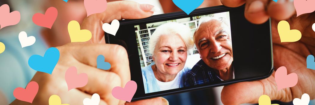 Illustrative image of colorful heart shapes against senior couple taking a photo from mobile phone