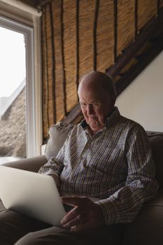 Side view of a senior man using laptop while sitting on a sofa in living room at home