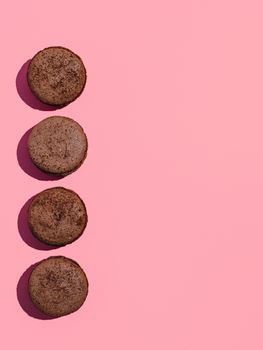 Chocolate macarons with copy space. Row of perfect french macarons or macaroons on pink background. Top view or flat lay. Hard light