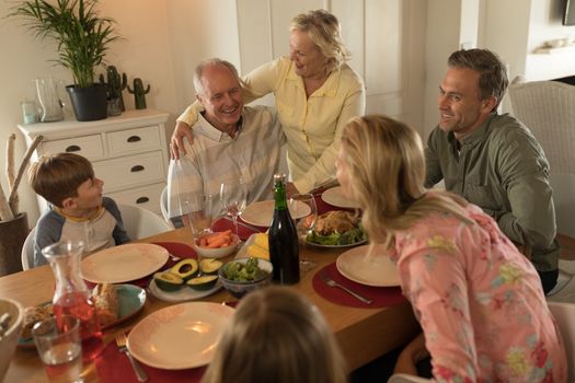 Side view of a multi-generation family interacting with each other while having meal on dining table at home