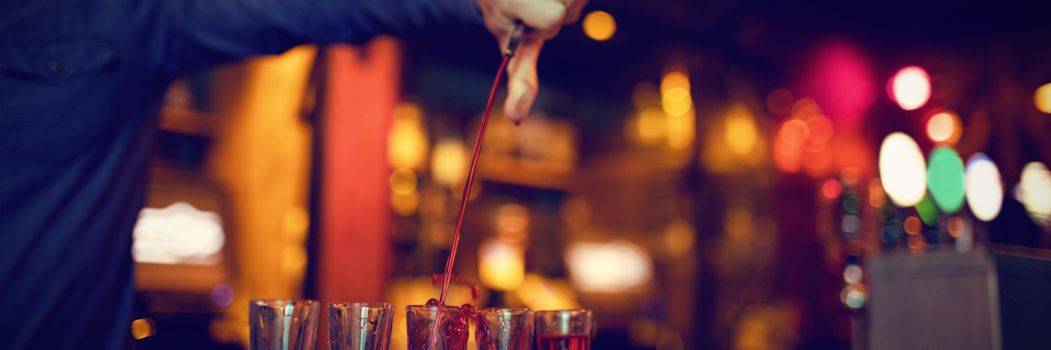 Bartender pouring alcoholic drink in shot glasses at bar