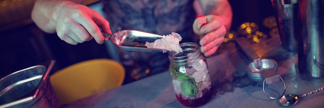 Bartender putting ice in jar while preparing cocktail at bar