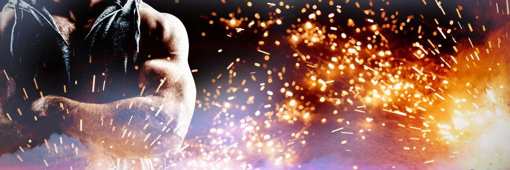 Handsome bodybuilder with arms crossed against firework bursting sparkle background