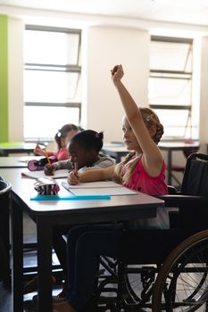 Side view of disable schoolgirl raising hand in classroom of elementary school