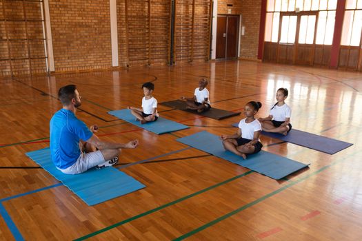 Side view of yoga teacher teaching yoga to school kids in school gymnast