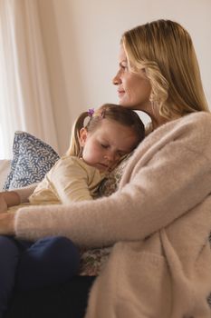 Side view of smiling mother embracing her sleeping daughter in arms at home