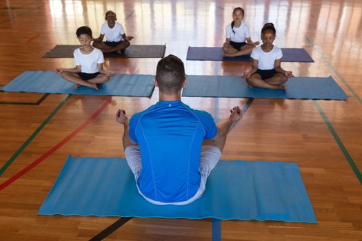 High angle view of yoga teacher teaching yoga to school kids in school gymnast 