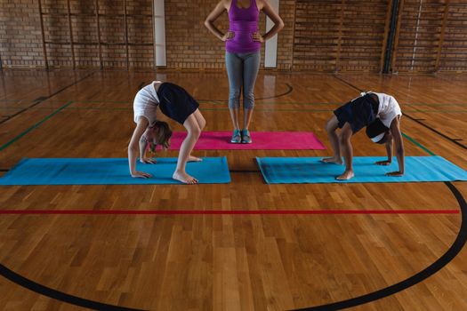 Front view of young female yoga teacher and schoolkids doing yoga on a yoga mat in school