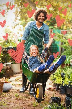 Red Hearts against cheerful man giving wheelbarrow ride to female gardener