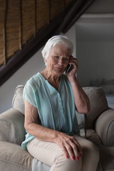 Front view of a senior woman talking on mobile phone while sitting on a sofa in living room at home