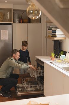Side view of father and son putting utensils in dishwasher at home