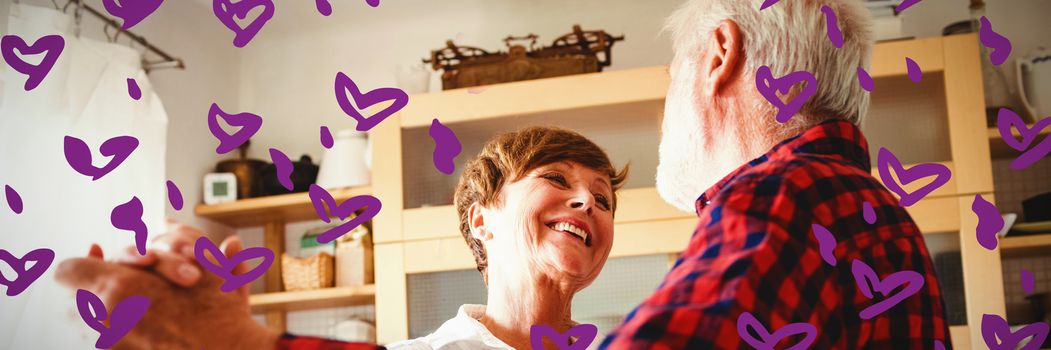 Heart shape purple paint on white background against senior couple dancing together in kitchen