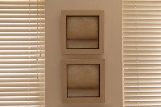 Front view of modern wall frames fixed on a cream wall between two window blinds at home