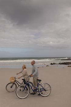 Side view of active senior couple walking with bicycle at the beach with ocean in the background. Theys seem happy