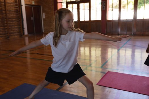 Front view of schoolgirl doing yoga position on a yoga mat in school gymnast 