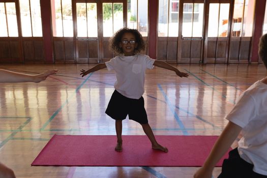 Front view of schoolgirl doing yoga with smile on a yoga mat in school