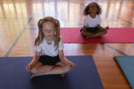 Front view of schoolgirls doing yoga and meditating on a yoga mat in school gymnast