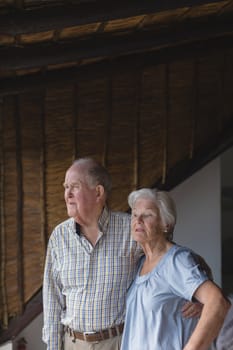 Side view of an active senior couple standing together and embracing each other while looking away at home