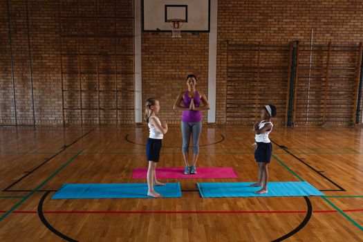 Front view of young female yoga teacher teaching yoga to school kids in school