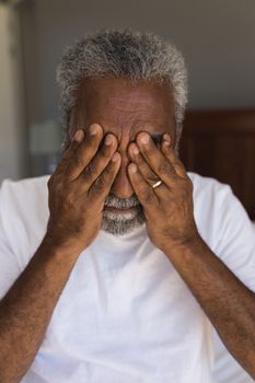 Portrait of a worried senior African American man covering his eyes in bedroom at home