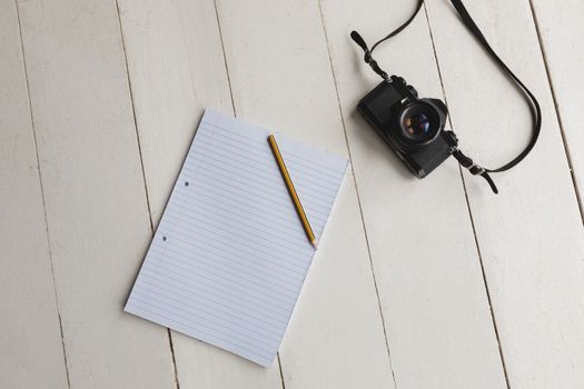 Overhead view of a notepad, pencil and camera placed on the floor at home