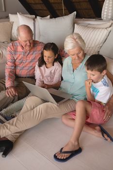 Front view of a multi-generation family using laptop on the floor of the living room at home