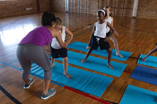 Young female yoga teacher teaching yoga to school kids in school