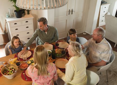 rear view of a multi-generation family interacting with each other while having meal on dining table at home