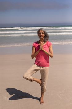 Front view of senior woman with eyes closed and hands clasped doing yoga on beach in the sunshine
