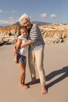Font view of happy senior woman embracing her granddaughter on beach in the sunshine