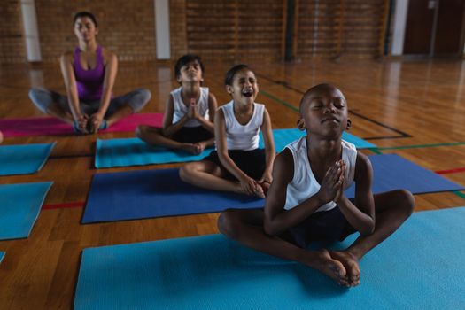 Front view of female yoga teacher and schoolkids doing yoga and meditating on a yoga mat in school