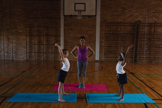 Front view of young female yoga teacher teaching yoga to school kids in school