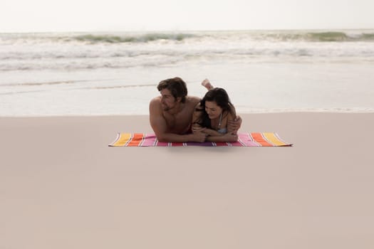 Front view of romantic young couple relaxing on blanket at beach in the sunshine