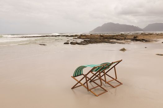 Side view of empty sun lounger chairs at the beach with mountains and ocean in the background
