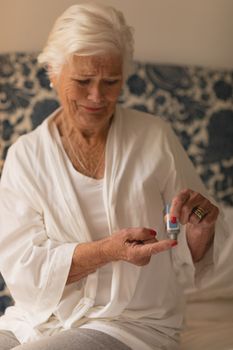 Front view of a senior woman applying cream on her finger in bedroom at home