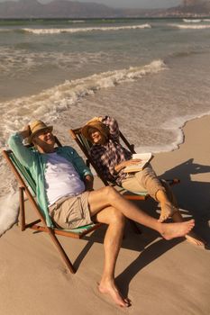 Side view of active senior couple having fun while relaxing on sun lounger at beach