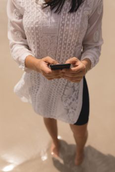 Low section of young woman using mobile phone on beach in the sunshine