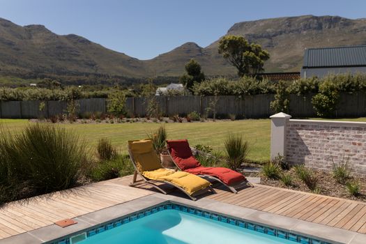 Empty sun lounger chairs placed next to the swimming pool at the backyard of home